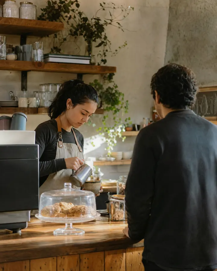 Barista prepara un café detrás de la barra mientras un cliente espera